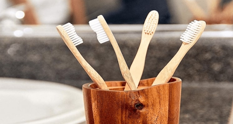 A wooden brush stand that holds a stack of wooden toothbrushes