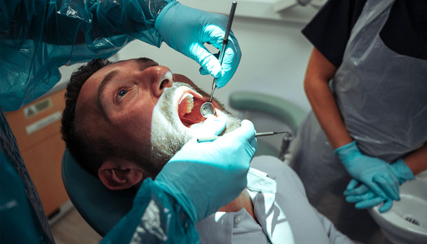 Dentist with male patient on reclining dental chair checking with mirror equipment for general Oral health at 4SquareDentistry