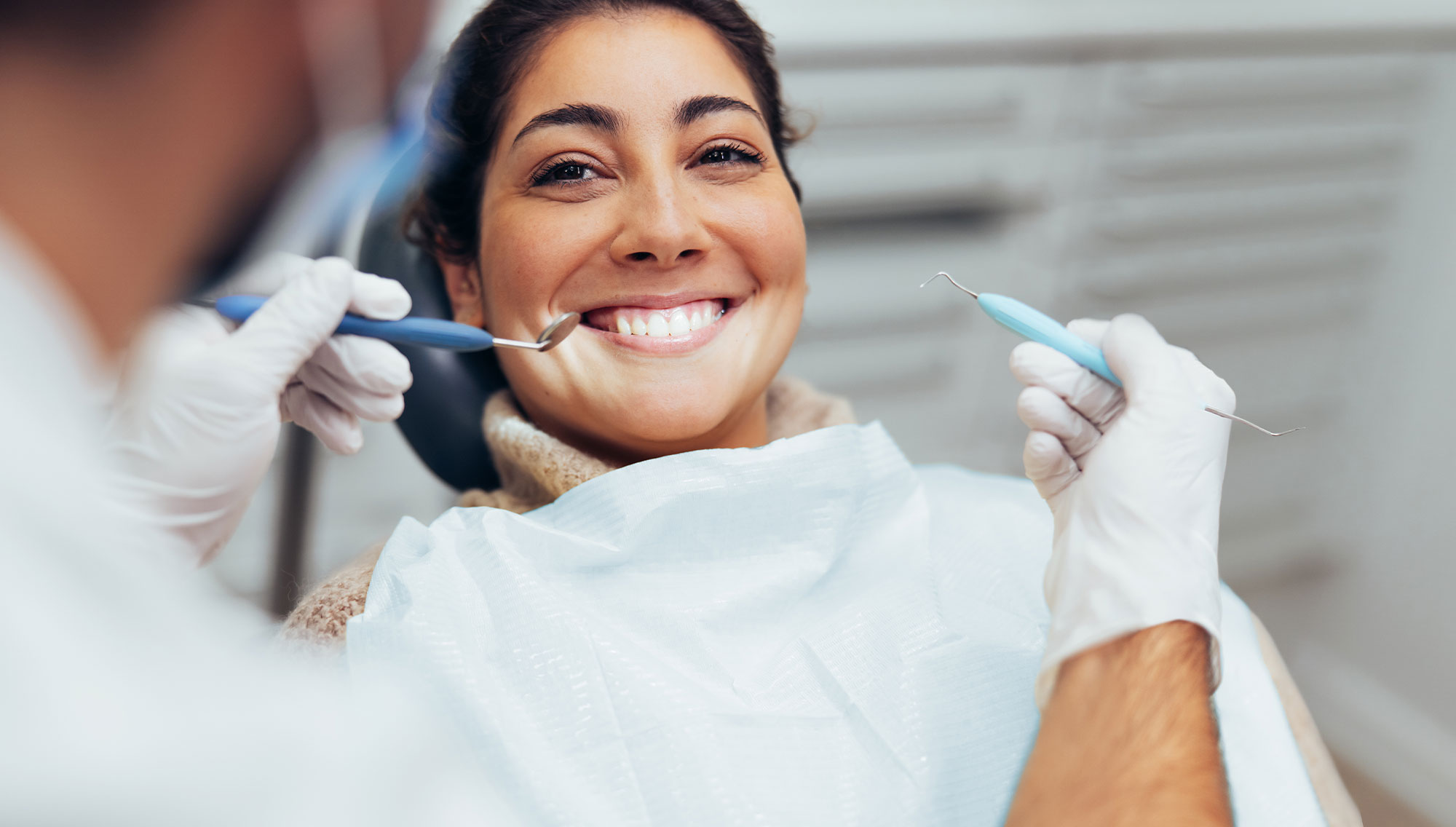 Pretty young smiling woman sitting in dental chair at dental clinic while dentist fixing her teeth