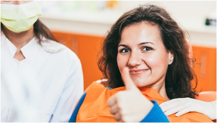 A women showing thumbsup and a smile with a nurse after a  oral surgery at 4 square dentistry