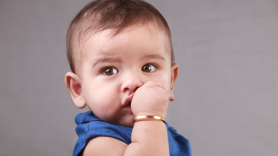 A baby with cute eyes is sucking his thumb by lying on bed captured by 4 SQuare Dentistry