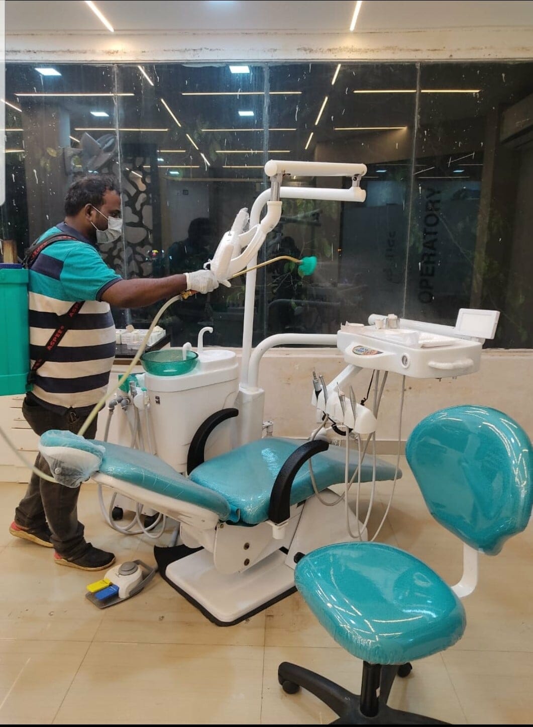 Using a disinfectant sprayer, a sanitation worker disinfects the dental clinic chair and tray