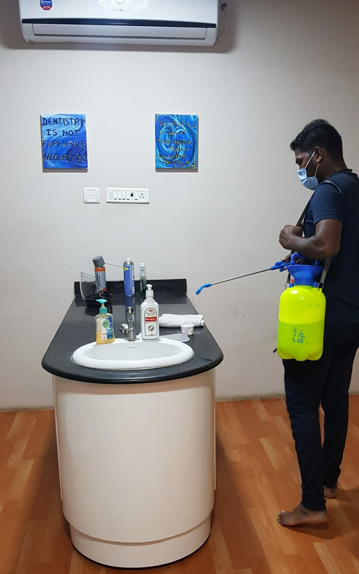 A sanitation worker cleaning the dental clinic work area with a yellow disinfectant sprayer
