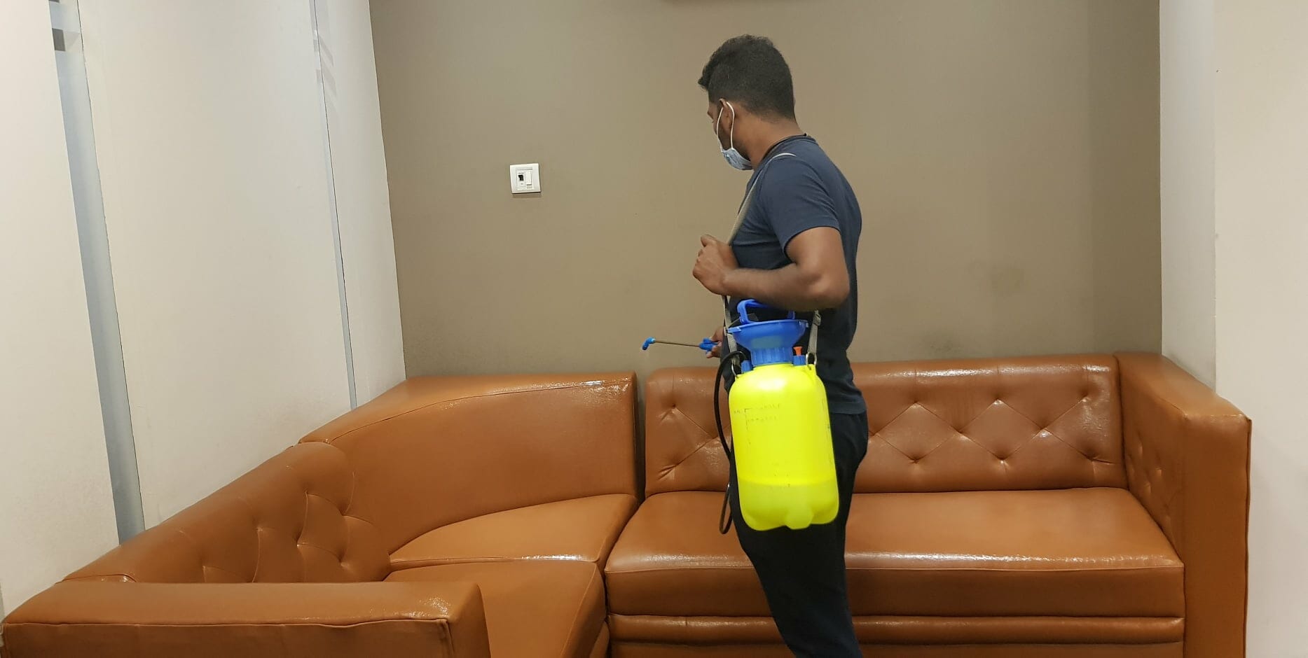 As part of a covid - 19 precautionary measure, a sanitation worker disinfects the dental clinic sofa