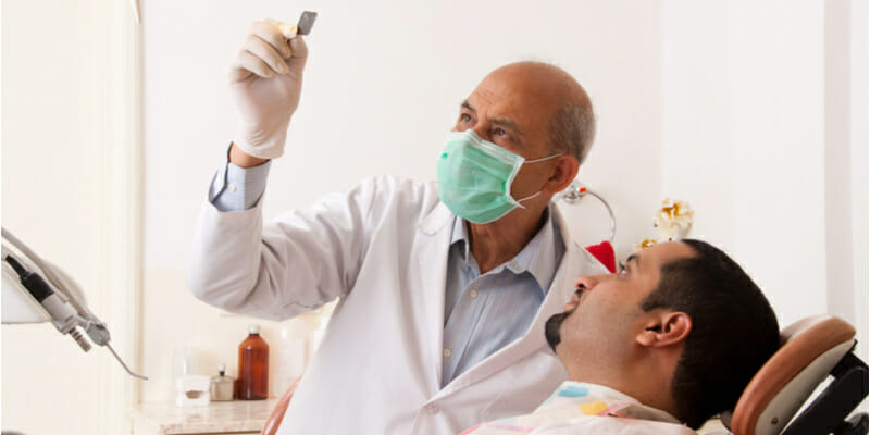 Senior dentist and male patient looking to dental x-ray before procedure, discussing the treatment in amodern dental clinic