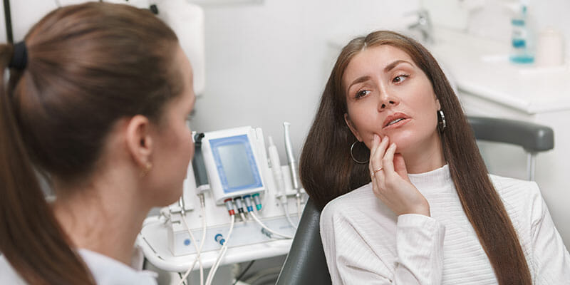 Dental clinic environment, attractive young woman patient explaining her toothache symptoms, female dentist listening to the patient
